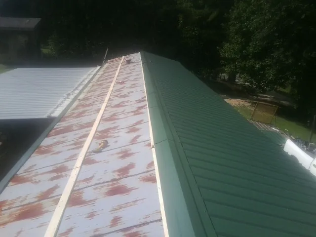 Old rusted panels beside newly installed green metal roofing in Burlington