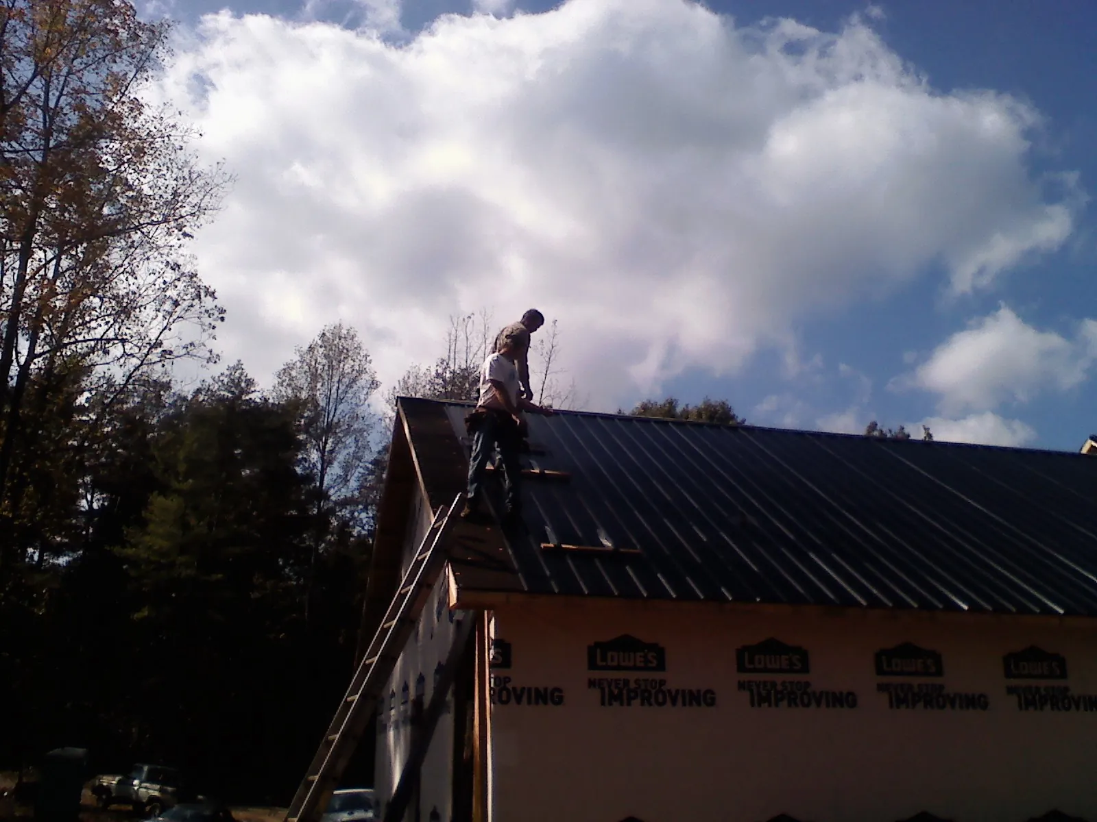 Roofer fastening dark metal panels high against a cloudy sky, from a Roof Inspection job in Burlington